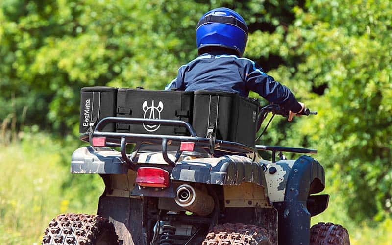 Man driving an ATV in the forest with ATV bags on his vehicle